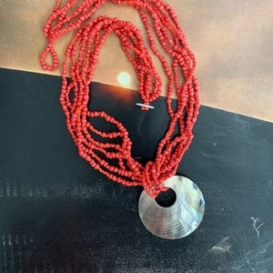 May include: A multi-strand necklace made of coral-colored beads with a large, round, white pendant.
