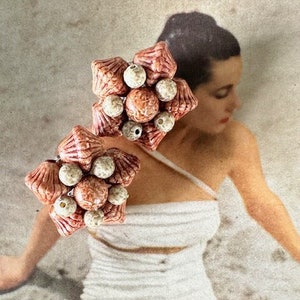 May include: A pair of vintage clip-on earrings featuring a cluster of pink and white ceramic flowers. The earrings are made of a textured material and have a delicate, feminine design.