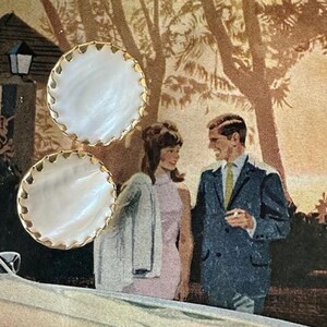 May include: A pair of white pearl earrings with gold scalloped edges. The earrings are round and have a smooth, glossy finish.