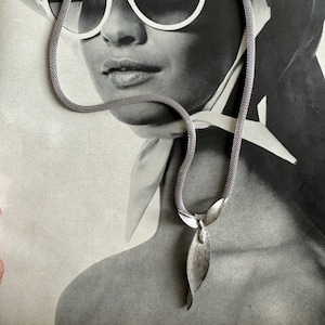 May include: A silver chain necklace with a leaf-shaped pendant. The necklace is made of a fine mesh chain and the pendant is a single, long, pointed leaf.