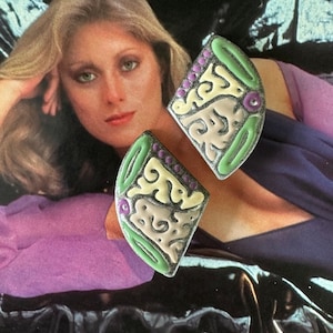 May include: A pair of vintage earrings with a geometric design. The earrings are made of metal and have a green, purple, and yellow enamel finish.
