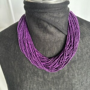 May include: A purple beaded necklace with multiple strands of small beads. The necklace is displayed on a black mannequin.
