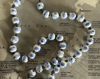 May include: A white and blue ceramic bead necklace with a blue string. The beads are decorated with a blue floral pattern. The necklace is laid out on a map of Japan.