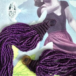 May include: A long purple beaded necklace with a button clasp. The necklace is made of many strands of small beads and is very long.