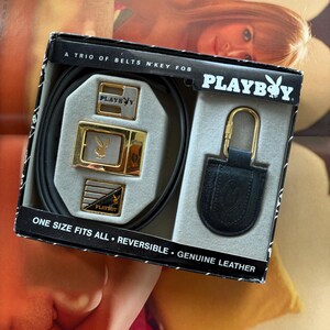 May include: A Playboy branded gift set in a black box containing a black reversible leather belt, three interchangeable gold and silver-tone metal belt buckles with the Playboy rabbit logo, and a black leather key fob with a gold-tone metal clip.