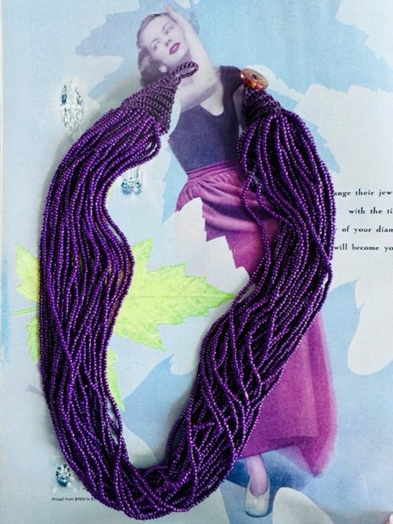 May include: A long purple beaded necklace with a tassel at the end. The necklace is made of small, round beads that are strung together in a long strand. The tassel is made of the same beads, but they are gathered together at the end of the strand.
