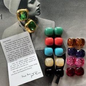 May include: A collection of colorful square and round earrings in various colors, including green, red, blue, and gold. The earrings are displayed on a vintage photograph of a woman. A handwritten note is also included.