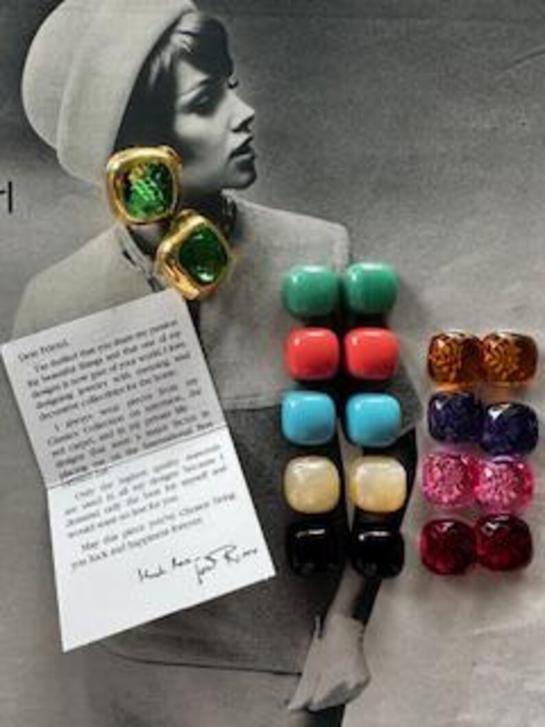 May include: A collection of colorful square and round earrings in various colors, including green, red, blue, and gold. The earrings are displayed on a vintage photograph of a woman. A handwritten note is also included.