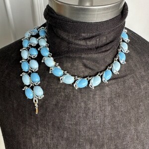 K&ouml;nnte beinhalten: Eine silberfarbene Halskette mit einem abgestuften Ombre-Design aus hellblauen und dunkelblauen ovalen Perlen.