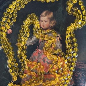 May include: A long, multi-strand necklace featuring translucent, yellow-gold circular beads. The necklace is draped over a vintage painting of a child in a historical costume. The beads are strung together, creating a layered effect.