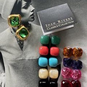 May include: A collection of vintage Joan Rivers Classics Collection earrings in various colors. The earrings are square or rectangular, with gold-tone metal settings. The image includes a pair of green gemstone earrings and a book with the text "Joan Rivers Classics Collection."