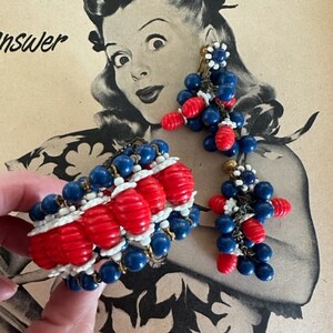 May include: A red, white, and blue beaded bracelet and earrings set. The bracelet is made of red, white, and blue beads and has a gold clasp. The earrings are dangle earrings with red, white, and blue beads.