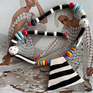 May include: A bold, colorful necklace with a geometric design. The necklace features black and white striped elements, along with red, blue, yellow, and orange beads. The background includes a vintage fashion magazine image.