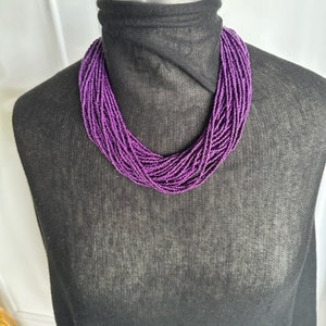 May include: A purple beaded necklace on a black mannequin. The necklace is made of many small beads that are strung together in a long strand.