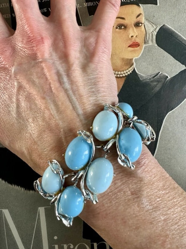 K&ouml;nnte beinhalten: Ein silbernes Armband mit blauen und wei&szlig;en Glasperlen. Das Armband befindet sich am Handgelenk einer Person.