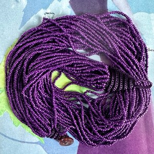 May include: A long strand of purple beads, made of small, round beads. The beads are strung together to form a necklace or bracelet.