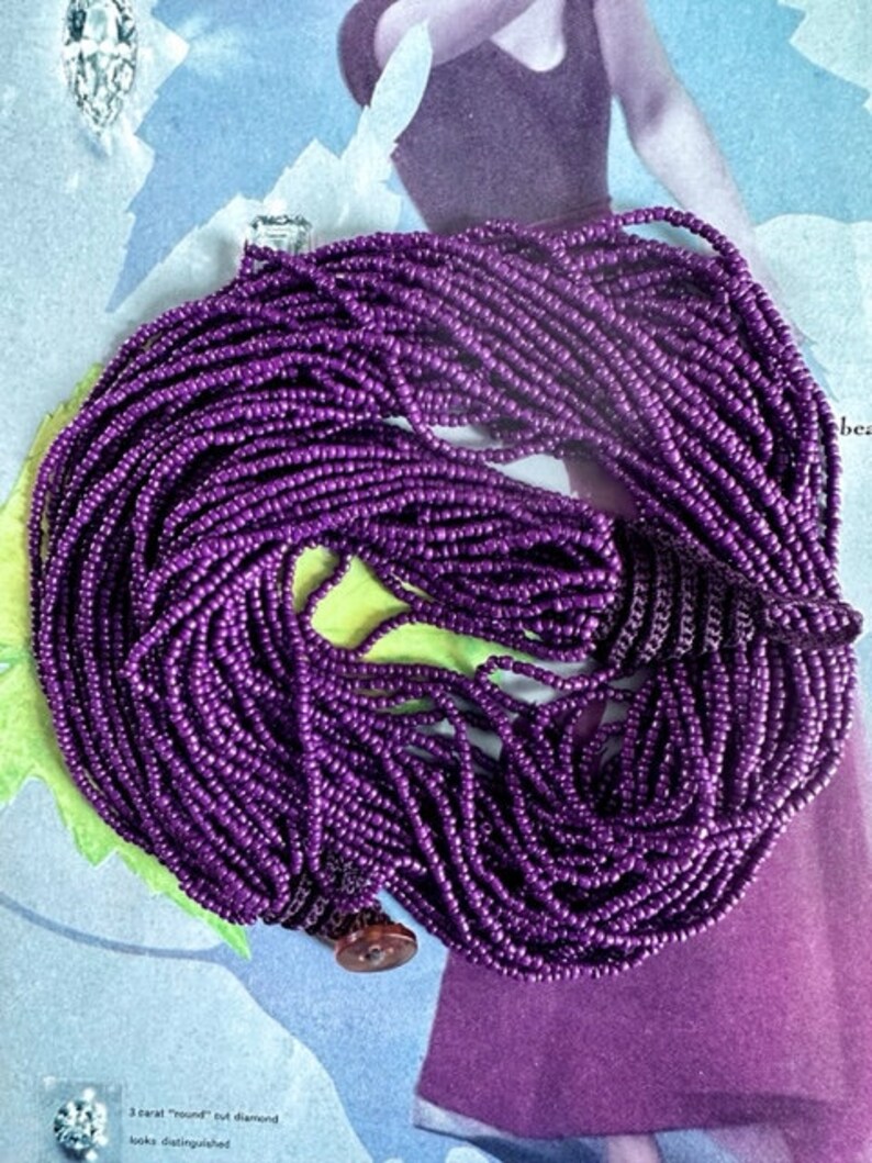 May include: A long strand of purple beads, made of small, round beads. The beads are strung together to form a necklace or bracelet.