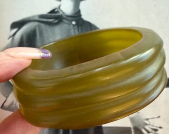 May include: Olive green, ribbed bangle bracelet. The vintage bracelet has a rounded shape with three prominent ridges. The background features a black and white image of a woman wearing a hat and coat. The words "look for fall" are visible.