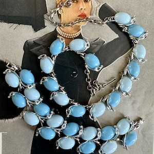 K&ouml;nnte beinhalten: Ein Vintage-Set aus Halskette und Armband in Silber mit hellblauen, ovalen Glassteinen. Halskette und Armband haben ein zartes Blumenmuster.