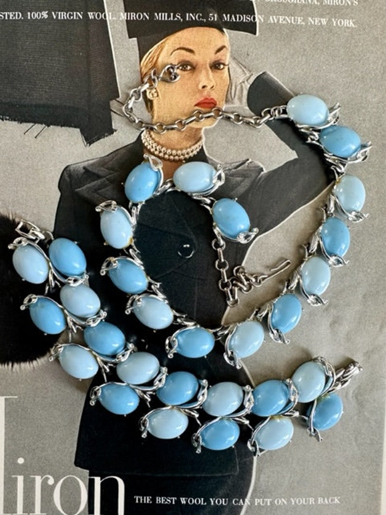 K&ouml;nnte beinhalten: Ein Vintage-Set aus Halskette und Armband in Silber mit hellblauen, ovalen Glassteinen. Halskette und Armband haben ein zartes Blumenmuster.