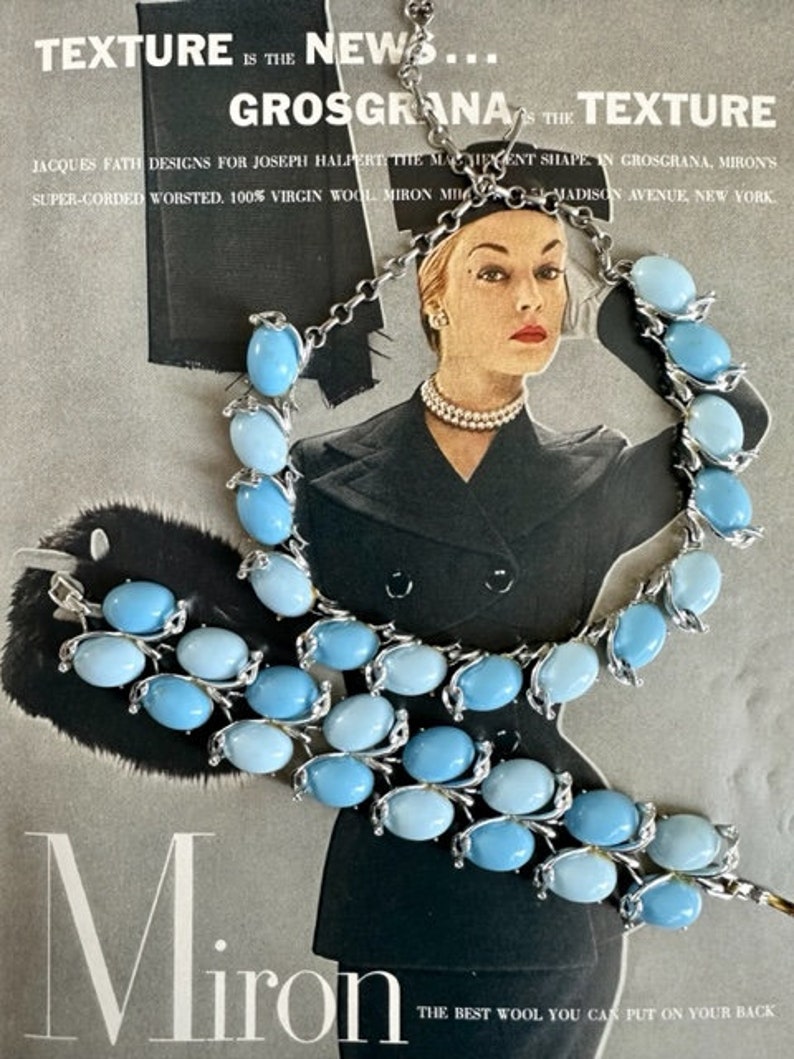 K&ouml;nnte beinhalten: Ein Set aus zwei blauen und silberfarbenen Halsketten mit ovalen Steinen. Die Halsketten liegen auf einem Magazin mit dem Text "TEXTURE IS THE NEWS... GROSGRANA IS THE TEXTURE" und "Miron THE BEST WOOL YOU CAN PUT ON YOUR BACK".