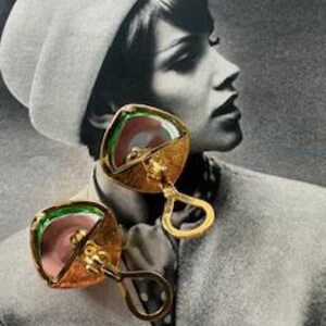May include: A pair of gold-toned, square earrings with a unique design. Each earring features a central pink element, surrounded by green and gold accents. The earrings have a distinctive handle-like shape, adding to their vintage appeal.