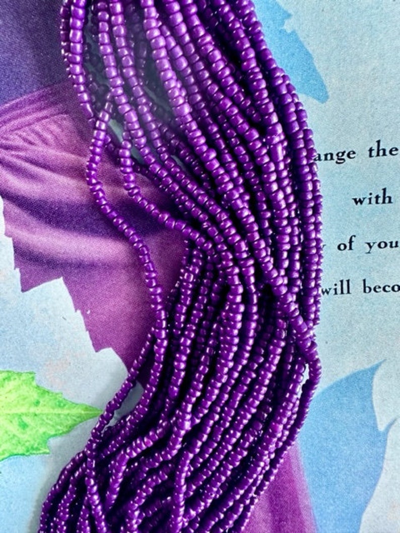 May include: A close-up of a strand of purple seed beads. The beads are small and round, and they are strung together in a long, continuous strand.