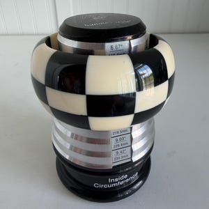 May include: A black and white checkered bangle bracelet displayed on a tiered sizing mandrel. The mandrel features printed measurements including 6.67 inches, 9.03 inches, and 9.42 inches, with the text Inside Circumference printed at the base.