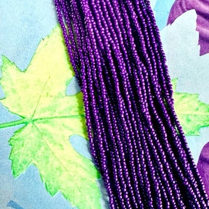 May include: A strand of purple seed beads, arranged in rows, against a colorful background.