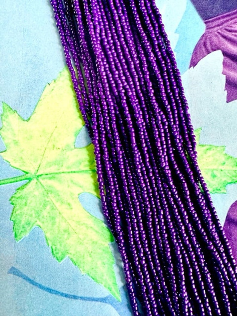 May include: A strand of purple seed beads, arranged in rows, against a colorful background.