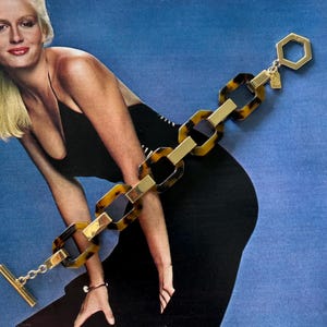 May include: A link bracelet featuring alternating tortoise shell patterned resin links and polished gold-tone metal rectangular bars. The bracelet includes a gold-tone hexagonal toggle clasp at one end and a matching gold-tone bar closure at the other.
