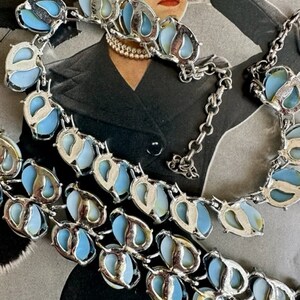 K&ouml;nnte beinhalten: Eine vintage silberfarbene Halskette mit blauen und wei&szlig;en irisierenden Steinen. Die Halskette besteht aus einer Kette mit einer Reihe von tropfenf&ouml;rmigen Steinen.