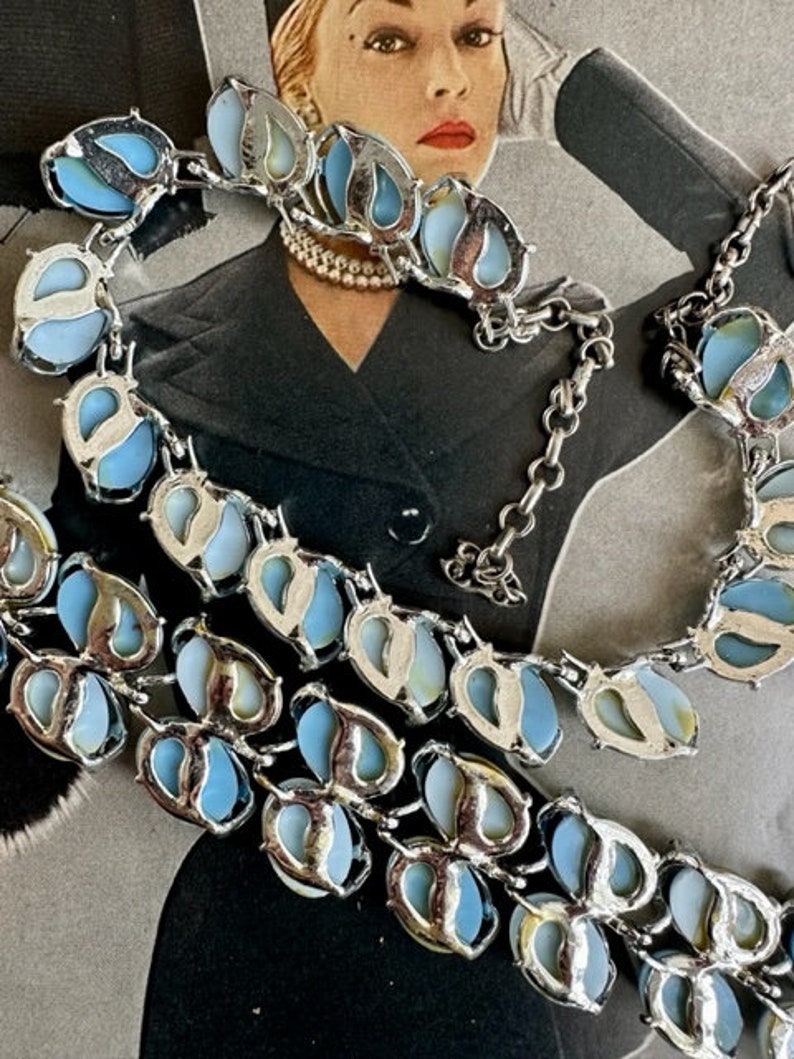 K&ouml;nnte beinhalten: Eine vintage silberfarbene Halskette mit blauen und wei&szlig;en irisierenden Steinen. Die Halskette besteht aus einer Kette mit einer Reihe von tropfenf&ouml;rmigen Steinen.