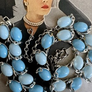 K&ouml;nnte beinhalten: Eine vintage Halskette aus blauen und hellblauen Glasperlen mit silberfarbenen Metallakzenten. Die Halskette besteht aus ovalen Perlen und hat einen Verschluss.