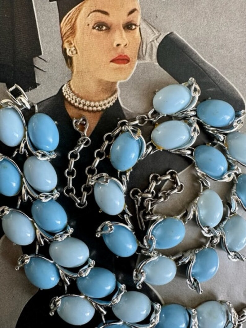 K&ouml;nnte beinhalten: Eine vintage Halskette aus blauen und hellblauen Glasperlen mit silberfarbenen Metallakzenten. Die Halskette besteht aus ovalen Perlen und hat einen Verschluss.