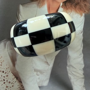 May include: A wide, chunky bangle bracelet featuring a high-gloss finish with a bold, repeating black and white checkerboard pattern. The bracelet has a rounded, thick profile and a smooth, polished surface that reflects light across its surface.