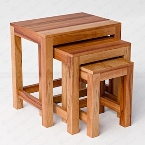 May include: A set of three nested tables crafted from natural light brown wood with visible grain patterns. Each table features a rectangular top and four straight legs connected by horizontal support bars near the base, arranged in descending size.
