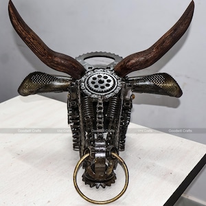 May include: A metal bull sculpture made from recycled materials. The sculpture features a detailed design with gears, chains, and springs. The horns are made of wood and the nose ring is made of brass.