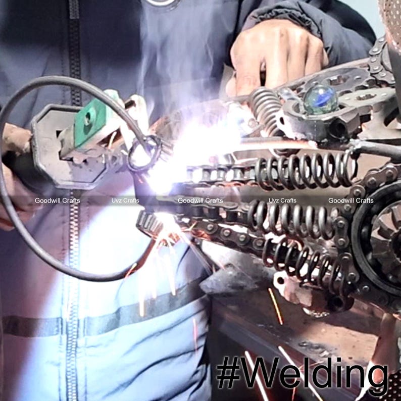 May include: A close-up of a person welding metal chains and gears together. The welding sparks are flying and the metal is glowing orange. The image is captioned with the hashtag #Welding.