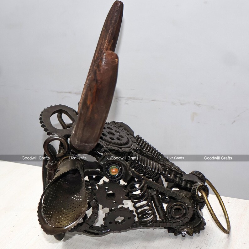 May include: A metal sculpture of a bull's head made from recycled metal parts, including gears, springs, and chains. The sculpture has a rustic brown finish and features a pair of wooden antlers.