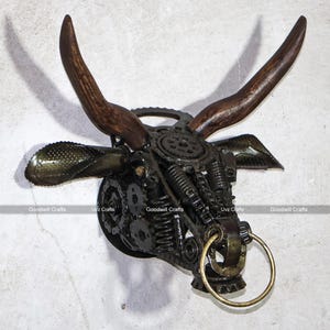 May include: A metal bull head sculpture made from recycled parts, including gears, springs, and chains. The horns are made of wood and the sculpture has a brass ring attached to the bottom.