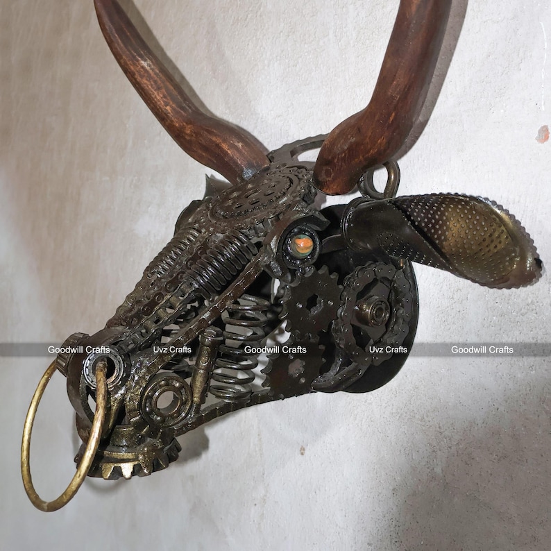 May include: A metal bull head sculpture with a wooden antler, made from recycled materials. The sculpture has a ring on the nose and a gear-like design.