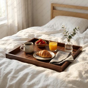 May include: A rectangular dark wood serving tray holds a speckled ceramic mug with dark liquid, a small wooden bowl of fresh red strawberries, a glass of orange juice, a croissant on a plate, and a clear glass vase with green eucalyptus stems.