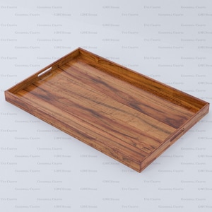 Pode incluir: Uma bandeja retangular de madeira com um acabamento castanho quente e rico. A bandeja apresenta uma superfície lisa e brilhante, com pegas integradas nas extremidades curtas. O veio da madeira é visível. Adequada para servir alimentos e bebidas.