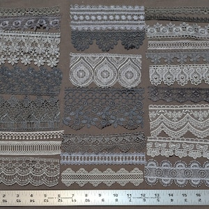 May include: Assortment of 18 different lace trims in black and white. The trims are arranged in rows on a brown fabric background. A ruler is included in the image for scale.