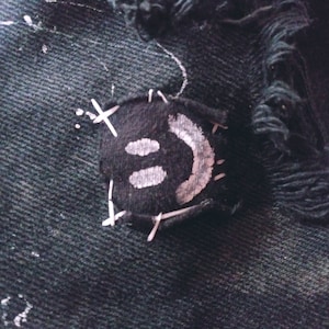 Peut inclure: Une veste en jean noire avec un patch smiley blanc cousu sur le devant. Le patch est cousu avec du fil blanc.