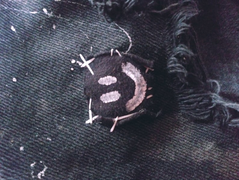 Peut inclure: Une veste en jean noire avec un patch smiley blanc cousu sur le devant. Le patch est cousu avec du fil blanc.