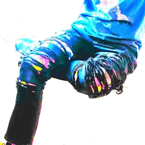 May include: Dark blue jeans with distressed detailing and colorful paint splatters. The jeans have a relaxed fit and feature ripped sections on the knees and thighs. The paint colors include pink, yellow, and purple.