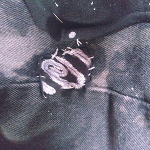 Peut inclure: Un gros plan sur un patch en tissu noir avec un motif en spirale blanc, cousu sur un tissu denim fonc&eacute;.