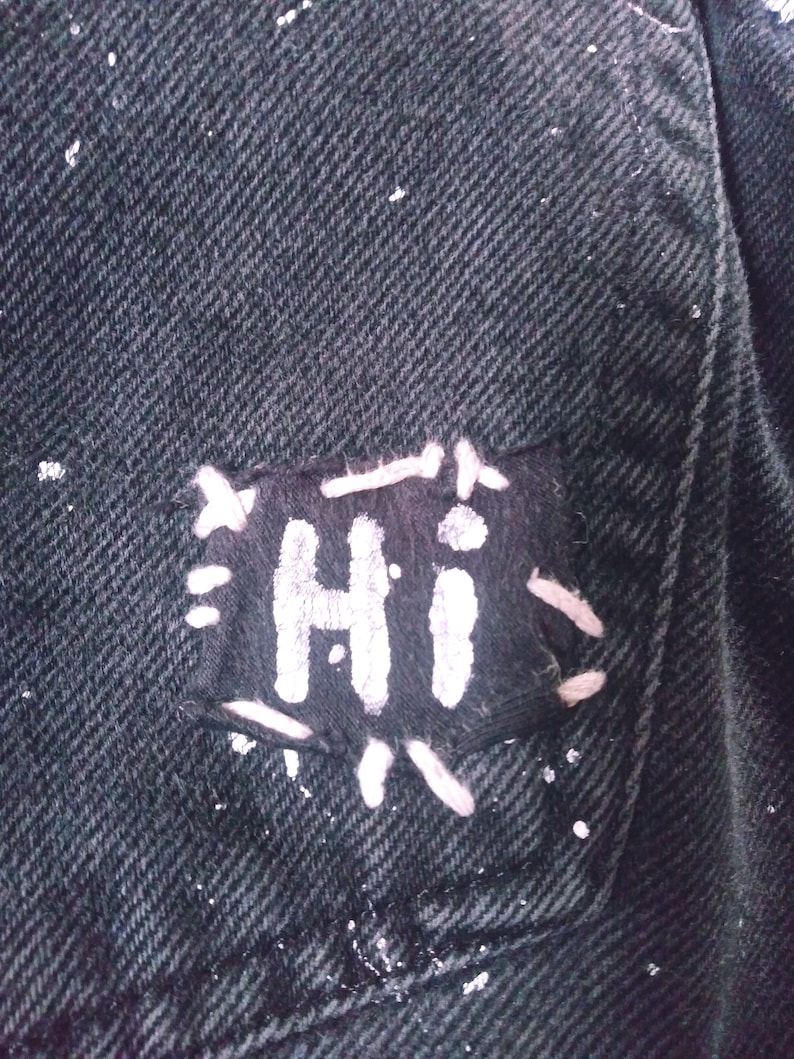 Peut inclure: Une veste en jean noire avec un patch brod&eacute; blanc qui dit "HI" dessus.